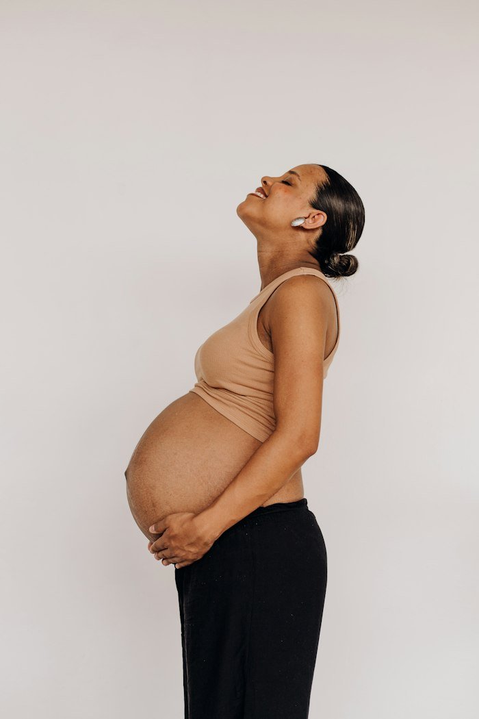 Pregnant woman standing in profile with her hands under her belly and her eyes closed, smiling